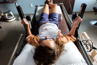 Girl lays in retrofitted hospital bed holding onto mechanisms that track her bimanual coordination