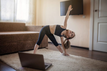 Girl watching online video on laptop and doing fitness exercises at home.
