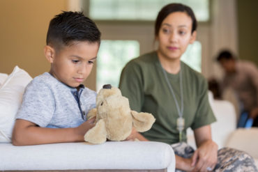 Elementary age boy plays with a stuffed animal, ignoring his mom who is about to leave for a military assignment.