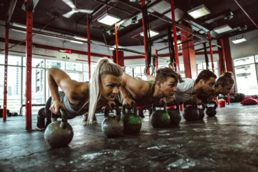 Group of four people perform kettlebell pushups in gym