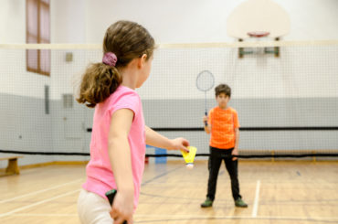 Two kids playing badminton in a gymnasium