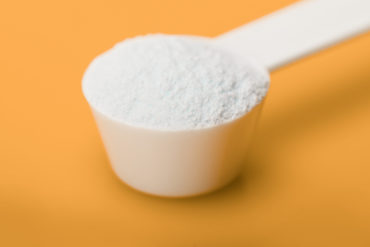 Creatine supplement in measuring cup against yellow background