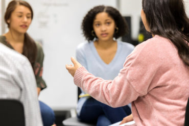 Side view of a teenage girl gesturing as she talks about something during a group workshop