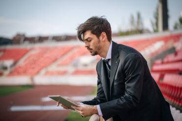 Sport team manager stands in empty stadium holding iPad looking frustrated