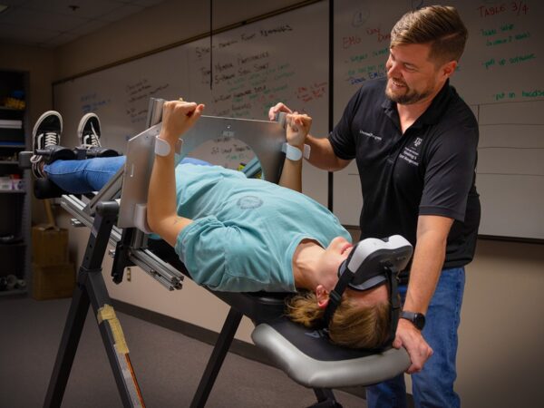 Member of SEHD's department of Kinesiology and Sport Management stands next to man laying down in bed as part of research procedure.