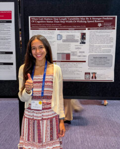Morales smiling and standing in front of a research poster titled "When Gait Matters: Step Length Variability May Be A Stronger Predictor of Cognitive Status Than Step Width or Walking Speed" at the American Science Biomechanincs conference.